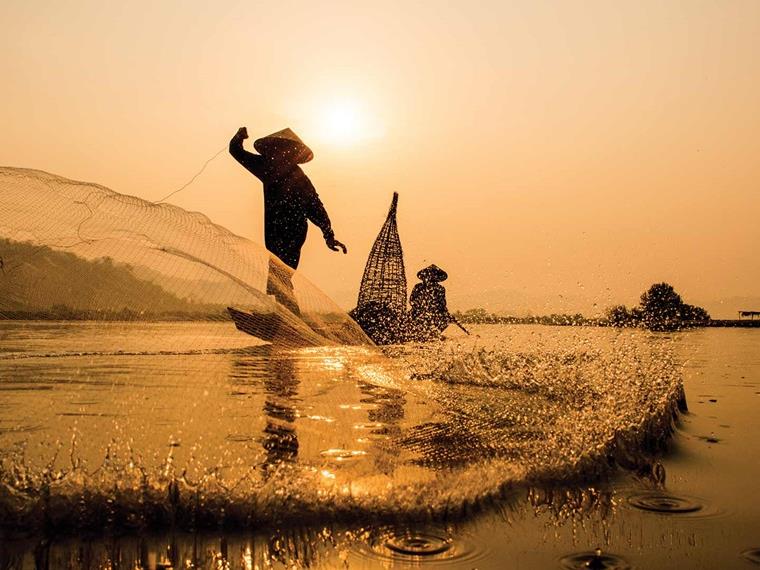 A traditional fisherman throwing a net at sunrise