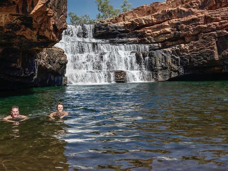 Two people swimming in water hole in front of waterfall, Australia